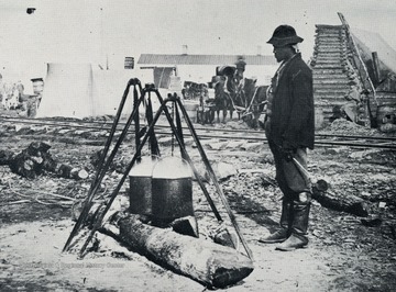 A Union Army cook watches two pots cooking over a fire.