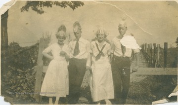 Donning party hats, a group poses outside. The inscription on the back of the photograph reads, "Blanche Cole, Fred Ramm, Evans, Myself, July 4, 1919, Just before we were married."