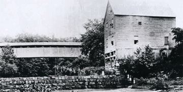 Caption reads: "In 1887 a covered bridge was constructed across Thirteen Mile Creek, at Buxton Mill in Mason County, just above the old mill. It was approximately 150 feet long and stood high above the waters of "Thirteen". An iron bridge replaced the old covered bridge in 1949. The old mill in the picture was built on Thirteen Mile Creek in 1877 by Darius Buxton. The large four story mill was the center of trade in that area. Picture and history furnished by Mrs. Juanita Burdette of Huntington, West Virginia."