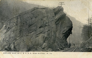 Man stands besides Bowlder Rock on the side of railroad tracks to emphasize it's size. See original for correspondence. Published by The Rose Company. (From postcard collection legacy system.)