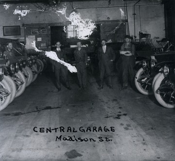 Several men stand in between lines of cars in a garage.