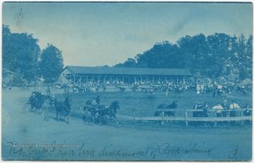 Men in uncovered carriages race their horses around the ring in front of the spectating crowd. (From postcard collection legacy system.)
