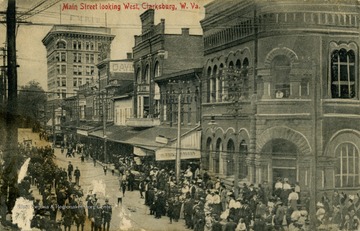 Procession is occurring down the middle of Main Street as on lookers watch. See original for correspondence. (From postcard collection legacy system.)