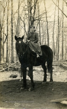 Young girl on horseback in the woods with her dog following behind. (From postcard collection legacy system.)