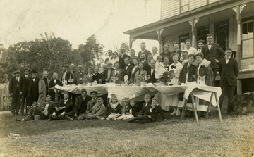 Large gathering outdoors around makeshift dinner table. (From postcard collection legacy system.)