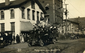 Truck filled with flag bearers travels down the road during Armistice Day celebration. (From postcard collection legacy system.)