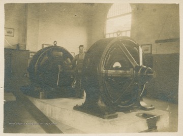 Worker stands between machinery inside of the Kingwood Power Station. (From postcard collection legacy system.)