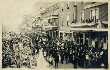 People gather in the streets to celebrate the Fourth of July. American flags hang all over the various buildings pictured. (From postcard collection legacy system.)