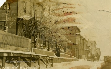 Woman stands on snow covered sidewalk, while horse and buggies make their way down snow covered 2nd Street. See original for correspondence. (From postcard collection legacy system.)