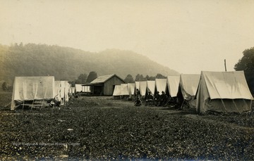 Group of soldiers sit outside of tent rows. (From postcard collection legacy system--subject.)