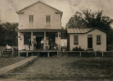 Several men stand on front porch of post office. Small horse and what appears to be a cow to the left of building.