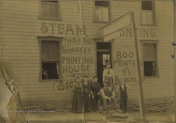 The two marked gentlemen, John Kiger and Brown Boughner, stand accompanied by unidentified persons in front of the largest printing house in the area.