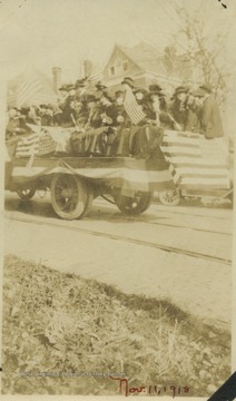 A large group of men and women squeeze into the back of the American flag covered truck smiling and waving flags of their own.