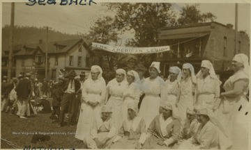 Group of nurses stand in front of "The American Legion" banner that hangs where the post office is now sited.