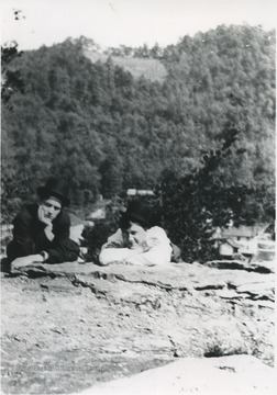 The two men pose on top of the rock with the town in the background.