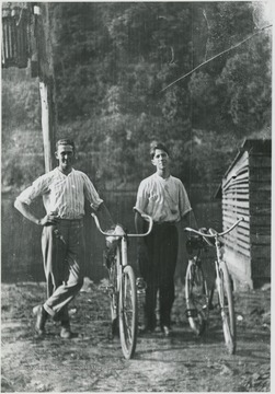 Two boys pictured with bicycles are pictured in front of the river. This picture was taken near Cooke Cabin.