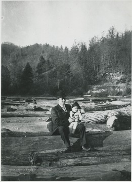 An unidentified man and his child sit on a cluster of logs. 