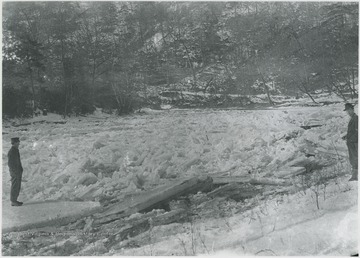Two unidentified men observe the frozen river. 