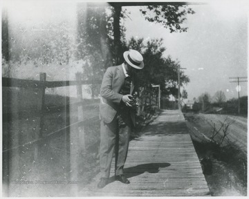 An unidentified man adjusting his camera on the sidewalk.