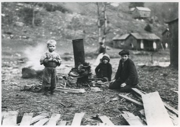 Three unidentified children pictured by rocks and scrap wood. 