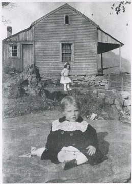 A child sits in the lawn. Subjects unidentified. 