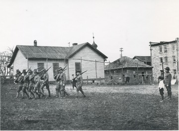 Enlisted soldiers run through a drill while supervised by a superior officer and a young boy who stands beside him. Subjects unidentified. 
