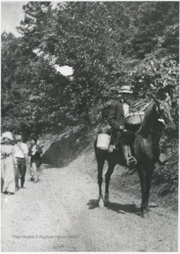A man on a horse rides down the trail while people walking trail behind. Subjects unidentified. 