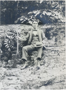 Hight pictured sitting on a log and holding a rifle. 