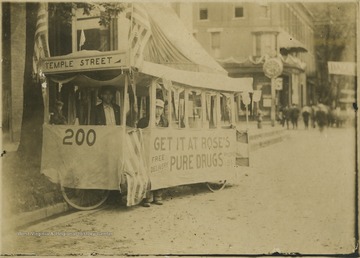 Two men stand inside the cart advertising "Get it at Roses's Pure Drugs". Subjects unidentified.