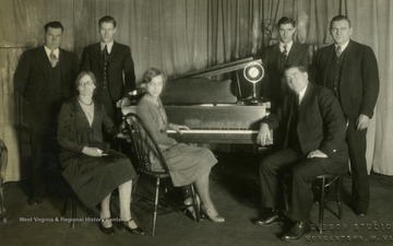 Print number 1602. Group of musicians pose next to a piano.
