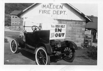 A car sits by  the Malden Fire Department with a sign that reads "Vote Rush Holt IN, State House Gang OUT". The photograph was most likely taken during one of Rush Holt's campaign's for state office.