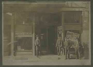 Four unidentified men pose by the building's entrance. The store windows advertise "American Field and Hog Fencing: For Sale Here" and "The Two Johns". This is became the location of Danny Foster's in 1986.