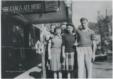 Pictured from left to right in the front is Earnett Cobb, Betty Jane Arrington Angell, and Lloyd Seldomridge. The two gentleman in the back are Homer Thrall, left, and Raymond W. Argabright. On the awning, above the group, reads, "The Gang's All Here".
