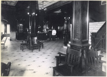 Interior of the hotel. An unidentified employee stands behind the counter next to a schedule of trains. 