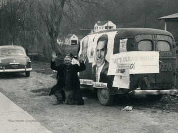 Man kneels beside van plastered in Dwight Eisenhower and Richard Nixon posters.