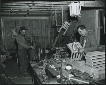 A man on the left repaints a sled while his colleague on the right put together a chair. The department had fixed toys and other items for less fortunate children during the holiday season. Subjects unidentified. 