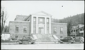 View of the building from across the street. A stray dog is pictured next to one of the parked cars.