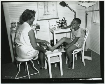 A nurse cares for a young boy's injured toe. Subjects unidentified. 
