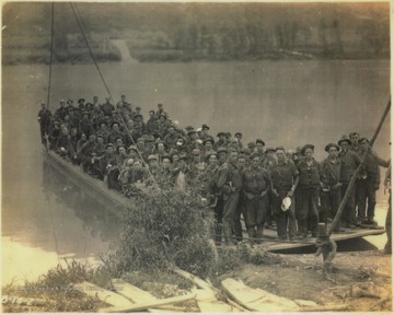 A group of unidentified workers from the Civilian Conservation Corps pose on the ferry which was built to cross New River to save workers the hassle of having to drive to Hinton and cross the river at the old toll bridge. The ferry then took the men up the Bluestone River where "the clearing of right of way was started", according tot he photo caption. 