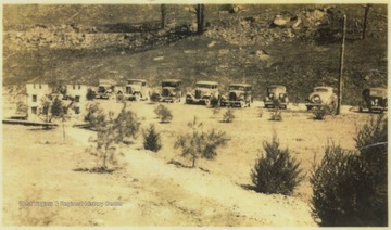Automobiles belonging to the army, forest service personnel, and corps engineers are parked along the dirt road. The insignia formation is pictured on the left. 