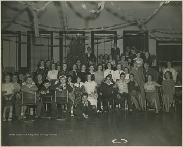 A group of kids ranging in age pose in front of a Christmas tree. 