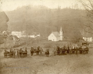 Lot Thomas is identified as being on horseback, and John Jobes is the tallest man (second from right). Second from left is probably Jim Simpson. Two additional men are identified as A.G. Henderson and M.H. Liming. The Methodist church in the background still exists in 2014 (the steeple was later removed). The house at far right was owned by Harley Staggers' family, later owned by Kenneth and Louise Wiley (it was demolished in the 1980s). Also, the building farthest in the background is a grist/sawmill built by John Rion Robinson, a civil war veteran and great grandfather of Jim Slade, a well known Morgantown resident. Few, if any of the other structures are extant, and a coal mine access road now occupies the hill in the background, which is heavily forested. See original for full note on back of photograph.