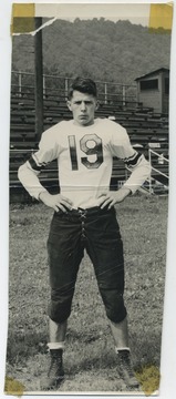 Persinger dressed in his uniform in front of the bleachers. The team mascot is the Bobcats. 