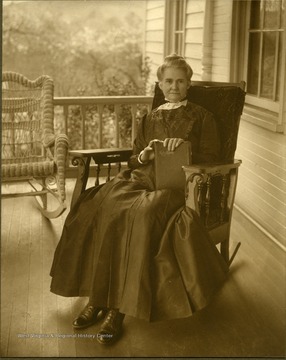 An unidentified elderly woman, attired in Victorian style clothes and hair, sits on a porch holding a Bible. She is possibly a member of West Virginia Governor Howard Gore's family.