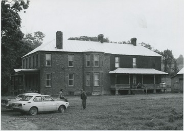 Two unidentified men are pictured by a parked car in front of the mansion.