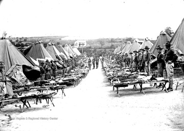 Soldiers at attention behind their cots covered in equipment.