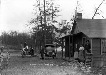 Horse and wagon as well as man next to automobile are parked outside building where several people stand on porch.