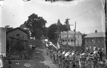 Soldiers marching band can be seen up front, followed by group representing Preston County coal miners. Little boy in bottom left watches the action.