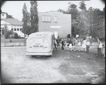 Students line up to catch a seat on the bus. Behind the line are teachers supervising. Subjects unidentified. 