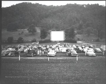 Automobiles cover the lawn in front of the movie screen. 